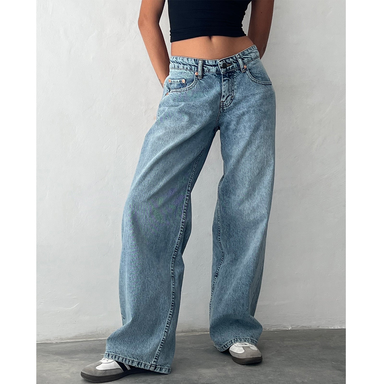Woman in light-wash blue high-waisted straight-leg wide jeans with black crop top, hands in pockets.