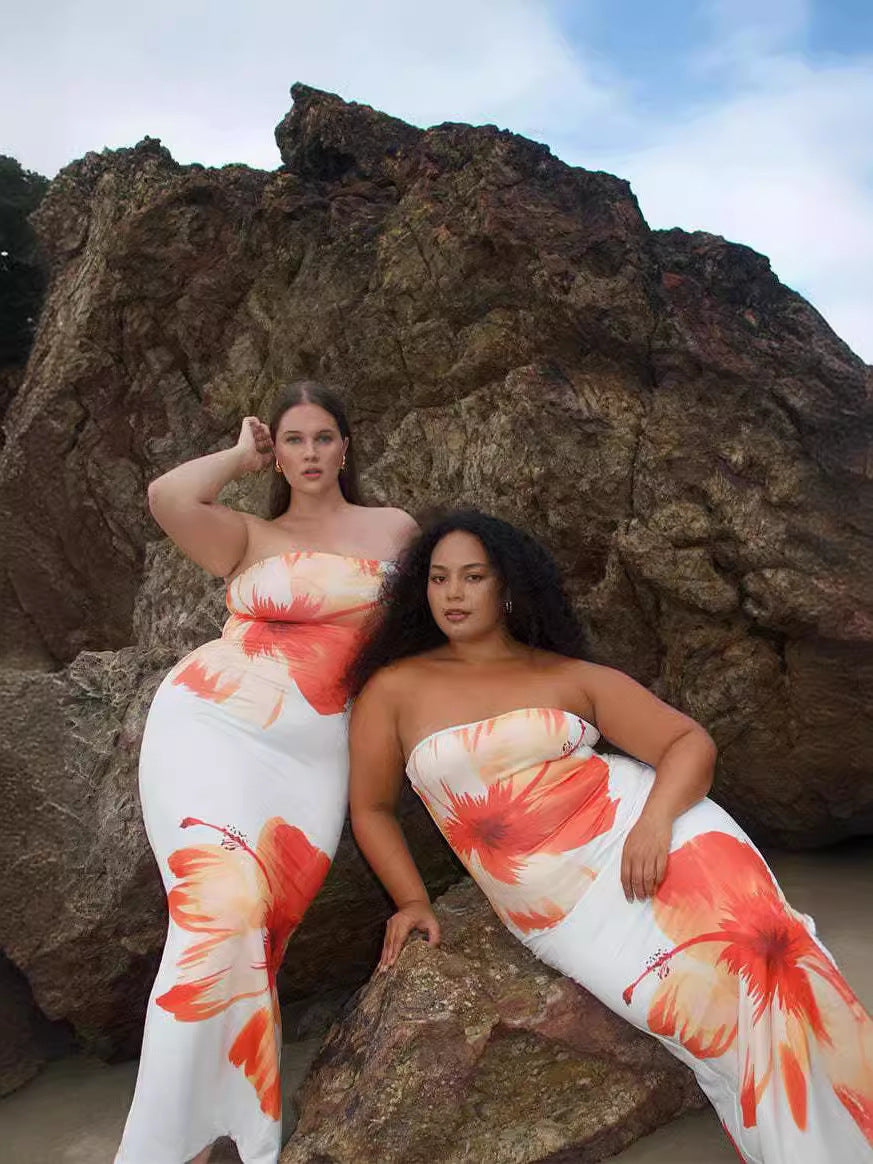 Two curvy models posing together in tropical Floral Print Long Dress, orange and pink blooms, rocky outdoor background.