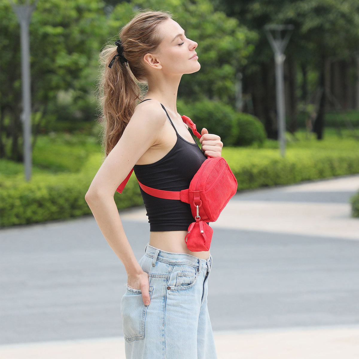 Side view of a woman wearing a red dog walking bag as a crossbody waist bag in a park