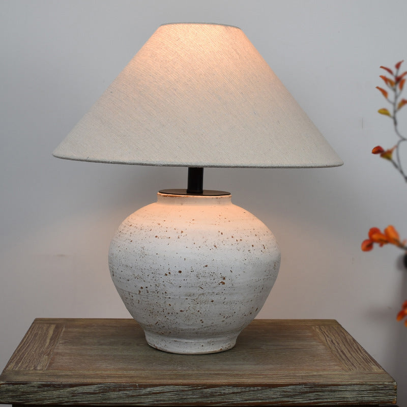 Mottled beige Japanese retro ceramic table lamp with textured base and fabric shade, lit on wooden tabletop with decor.