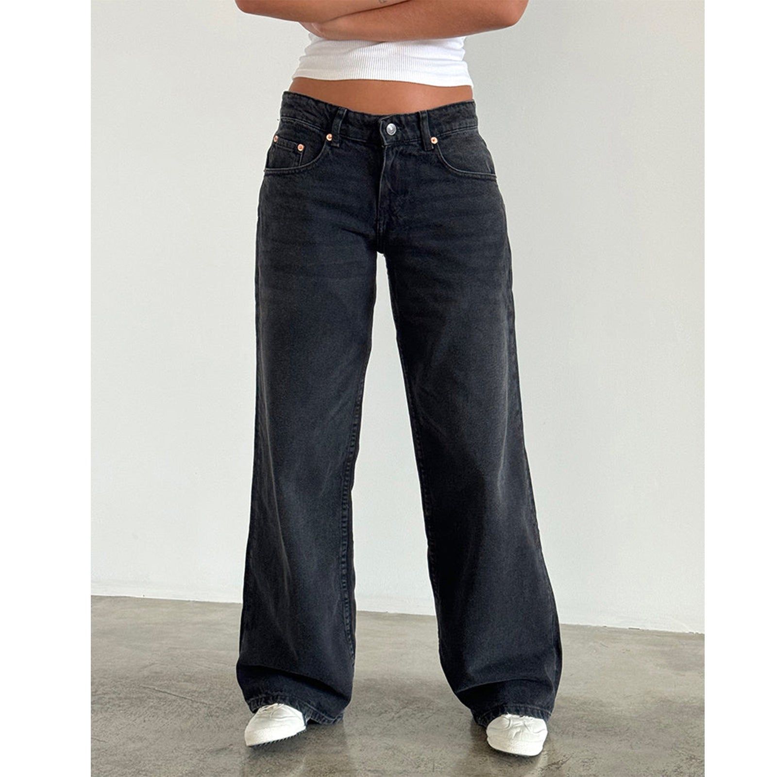 Woman in dark black high-waisted straight-leg wide jeans with white shoes and white top, front view.