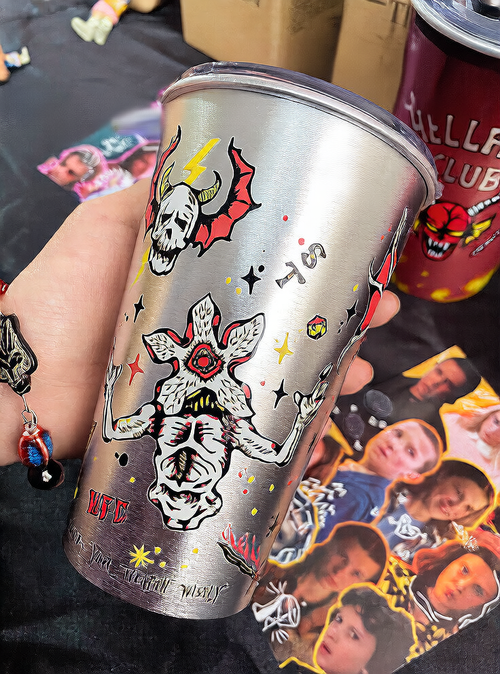 Color changing aluminum tumbler, demon skull style, held by hand with colorful background