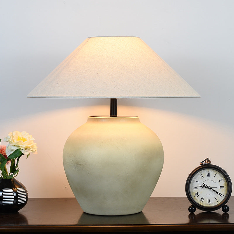 Vintage Japanese retro ceramic table lamp lit with warm glow, beige ceramic base and fabric shade, styled on nightstand with decor.