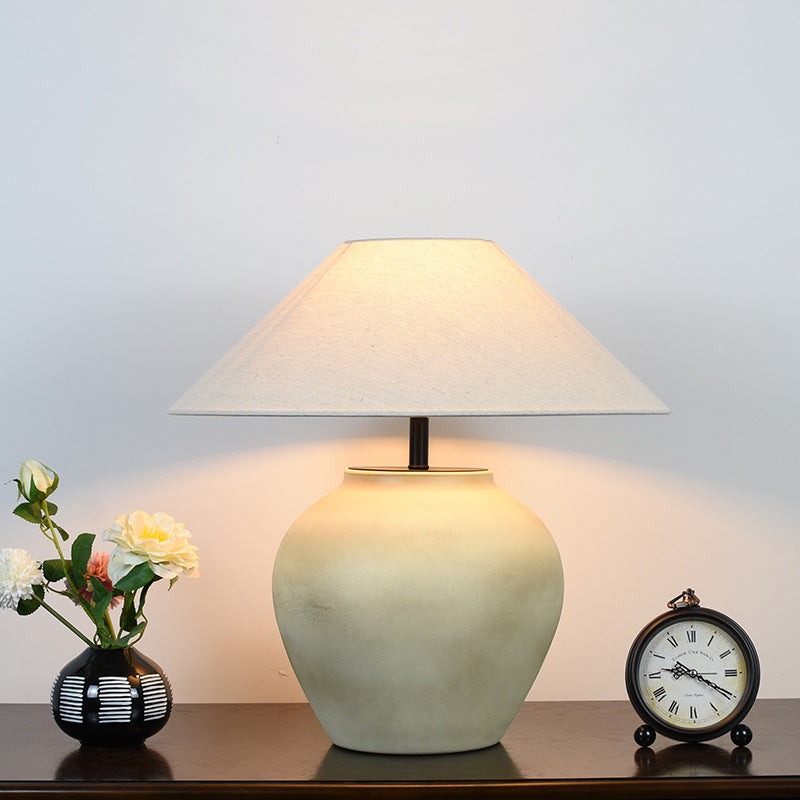 Lit beige Japanese retro ceramic table lamp with fabric shade, creating soft ambient light on bedside table setting