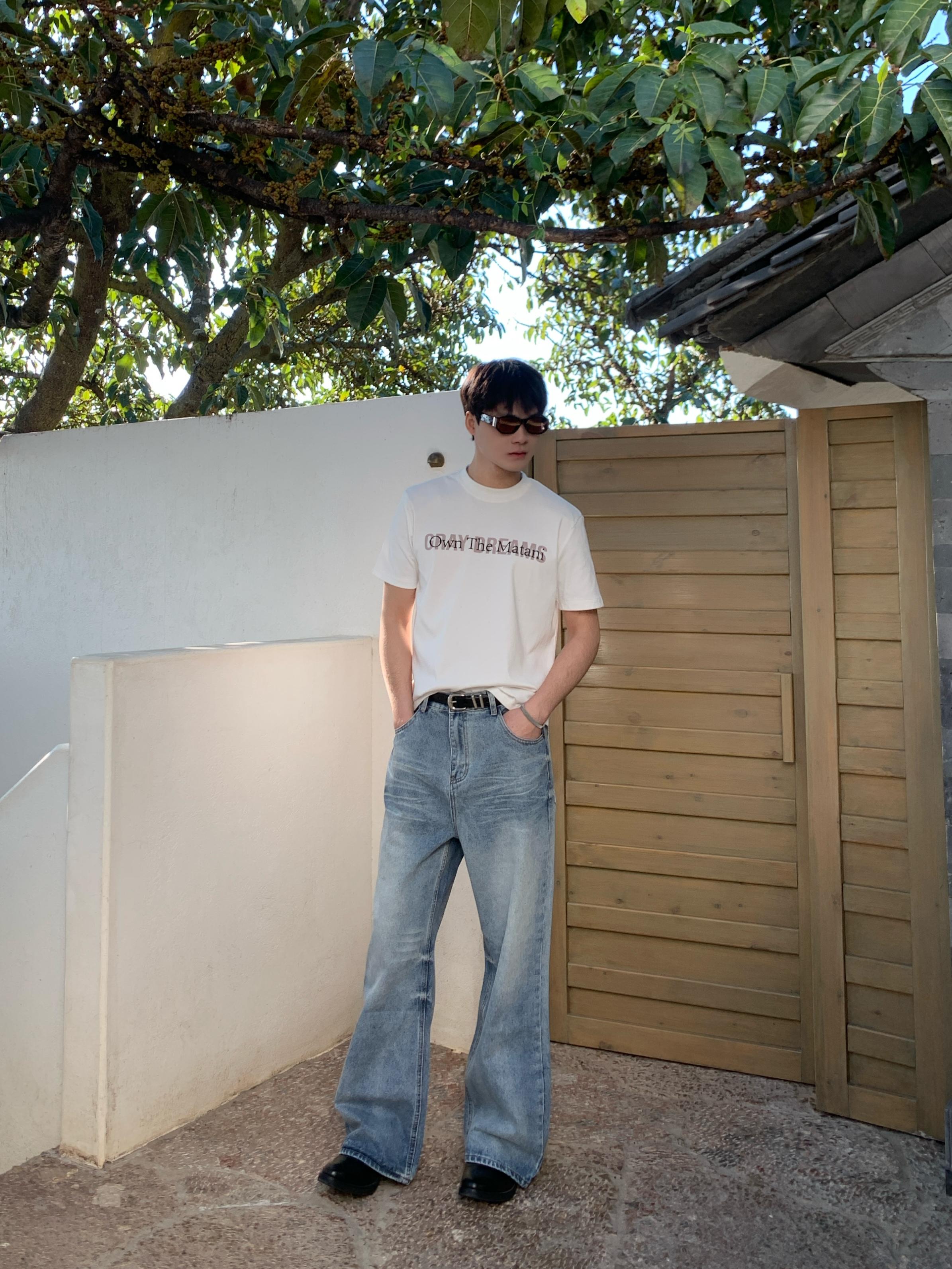 Side angle of model in loose fit blue baggy jeans showing wide leg silhouette and durable cotton fabric, outdoor setting.