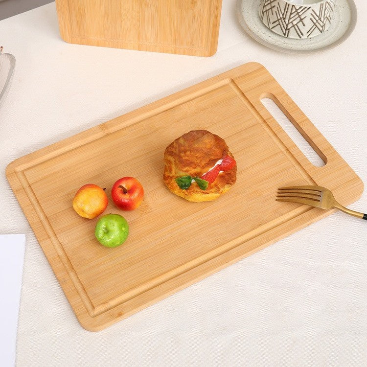 A bamboo cutting board holding a burger patty with toppings, fresh vegetables like tomatoes and lettuce, and a fork, arranged appetizingly on a surface.