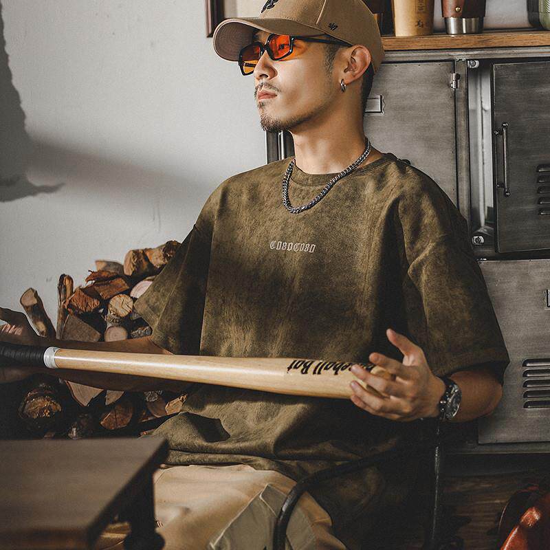 Oversized olive green suede T-shirt back graphic with ECHHERE branding, model in rugged pose holding baseball bat indoors