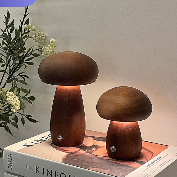 Two rechargeable wooden mushroom table lamps in dark and light wood finishes on a stack of books with greenery