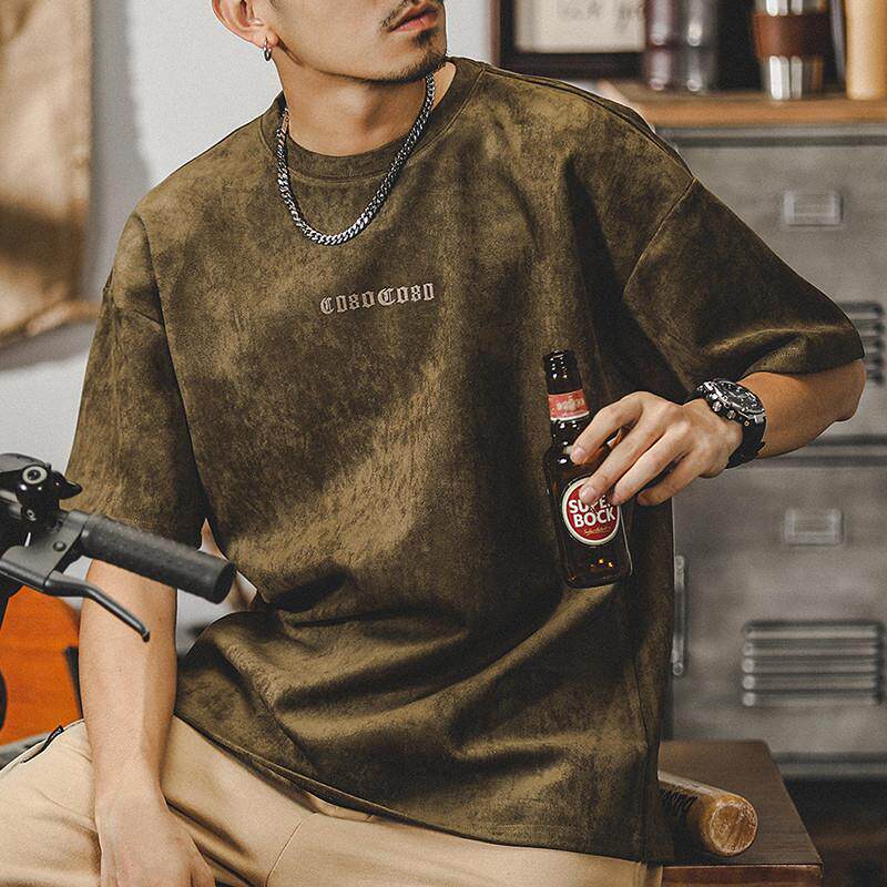 Suede T-shirt in earthy olive, relaxed fit on model sitting, subtle chest print, casual urban fashion vibe with bottle