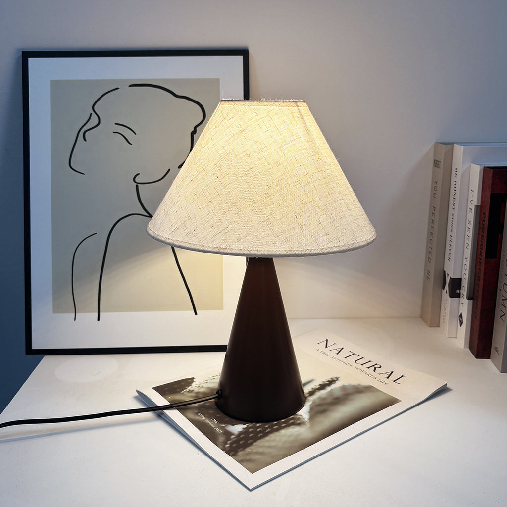 Vintage medieval table lamp with beige linen shade and dark metal base placed on a desk beside framed artwork.