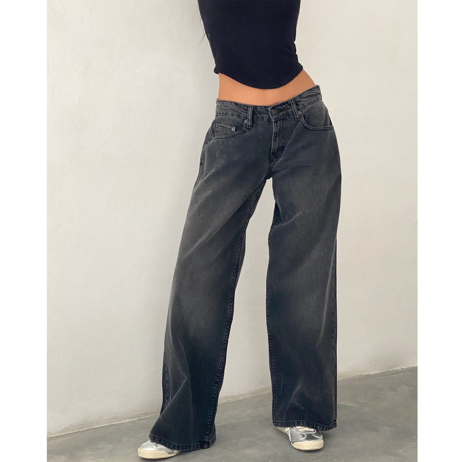 Woman in dark black high-waisted straight-leg wide jeans with white shoes, front view.
