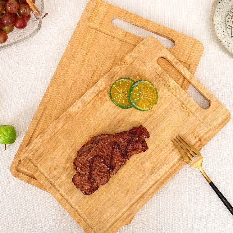 A large bamboo cutting board topped with a cooked steak, a fork, and some scattered lime slices and other small garnishes, placed on a table.