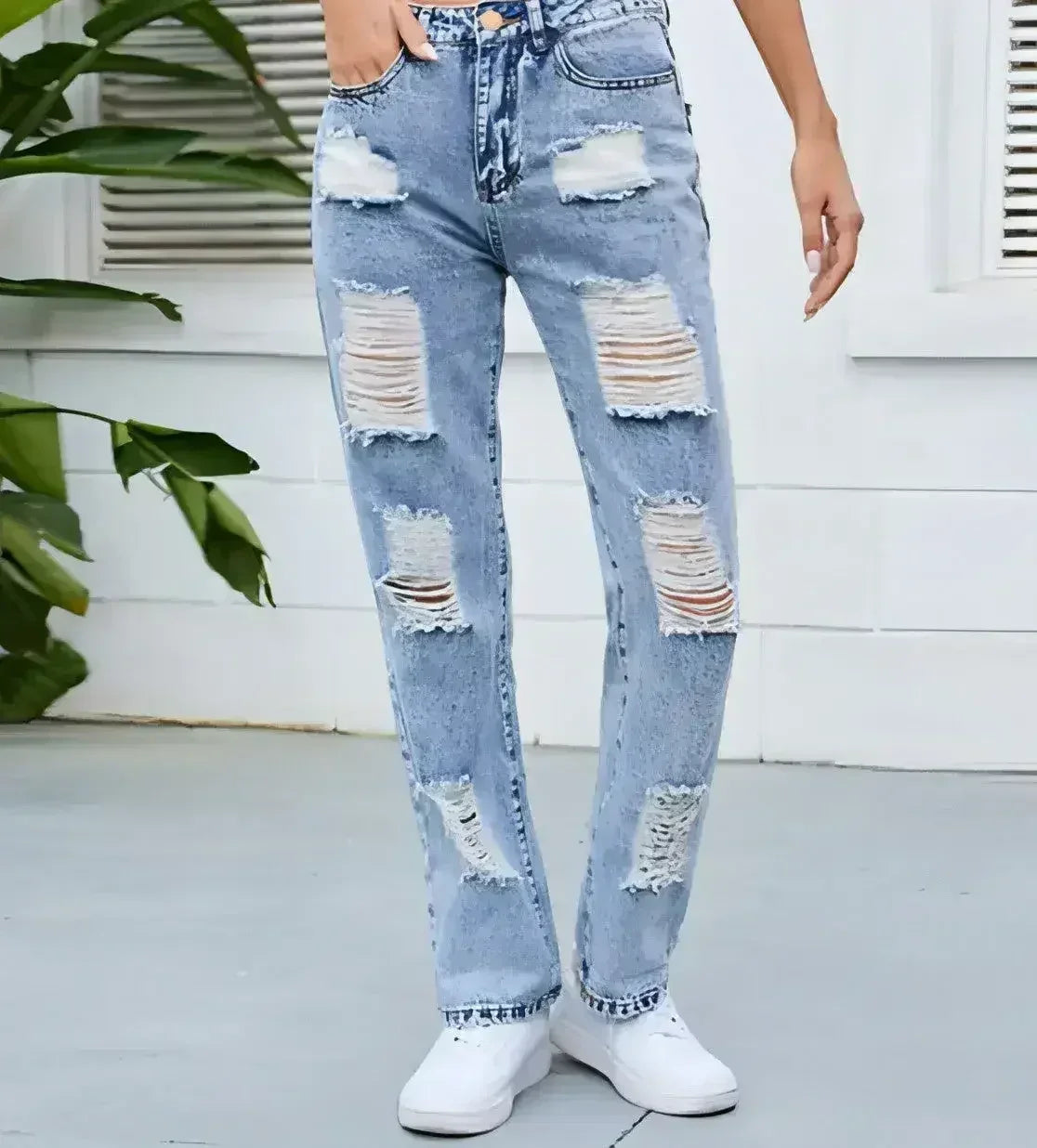 Close up front view of women’s ripped straight-leg jeans in light washed blue denim with heavy distressing