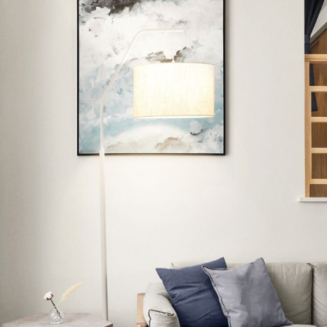Modern Nordic arc floor lamp with white body and white shade placed in bright living room beside sofa and artwork.
