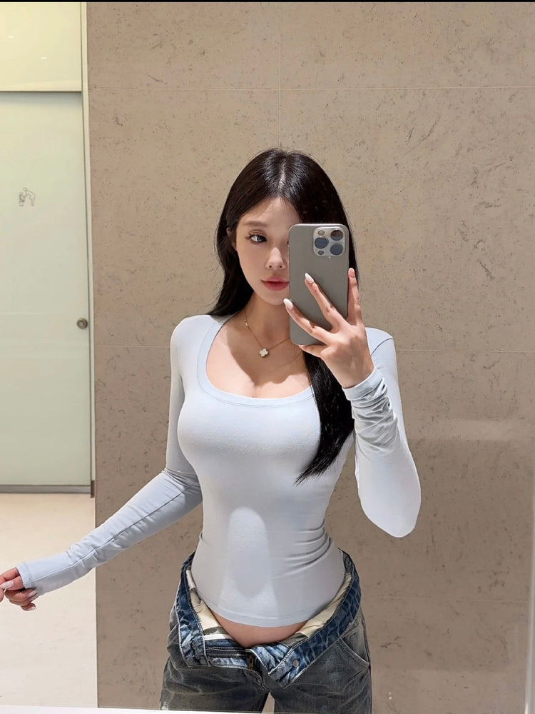 Woman in slim fit white long sleeve cotton spandex U-neck top taking mirror selfie, front view