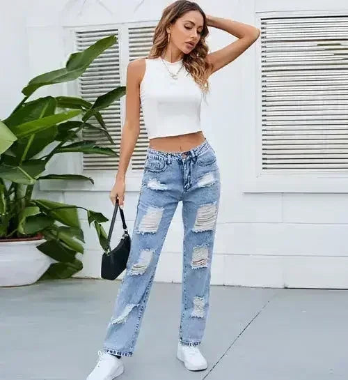 Women’s ripped straight-leg jeans in light blue worn with white crop top and black mini bag, casual streetwear outfit