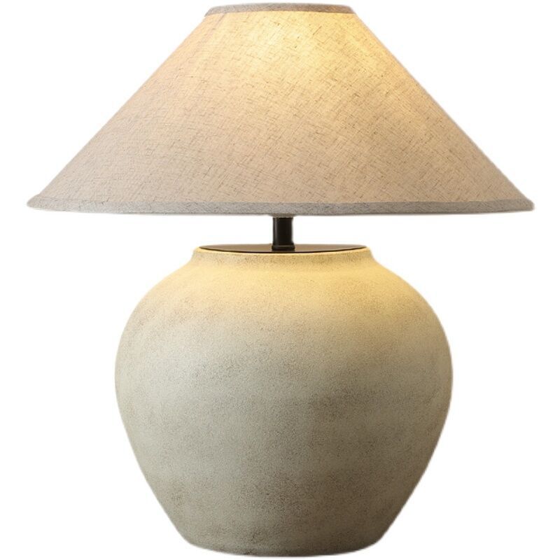 Vintage Japanese retro ceramic table lamp in beige, lit with warm light from fabric shade, three-quarter view on tabletop.
