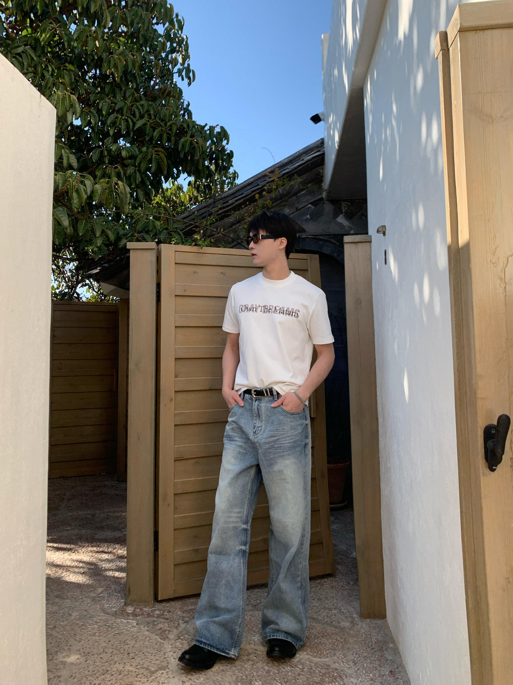 Full body shot of man in ice blue baggy jeans with button closure, relaxed fit, and vintage wash detailing, standing outdoors.