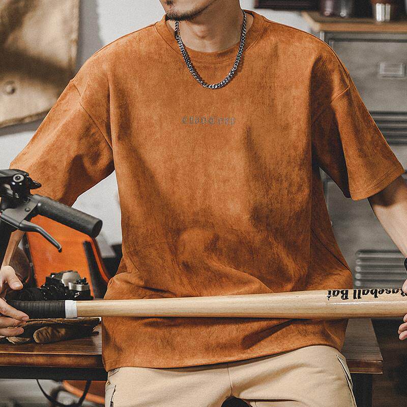 Dark olive suede T-shirt on young man, soft velvety finish, subtle ECHHERE chest print, indoor casual seated pose with chain necklace